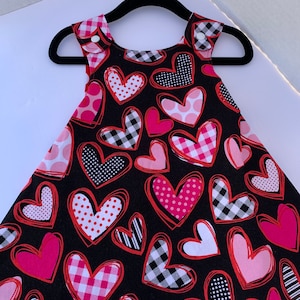 May include: A black sleeveless dress with a heart print. The hearts are pink, red, and white with different patterns, including polka dots, stripes, and plaid.