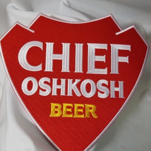 May include: Red embroidered patch with white text that reads "Chief Oshkosh Beer" in a shield shape.