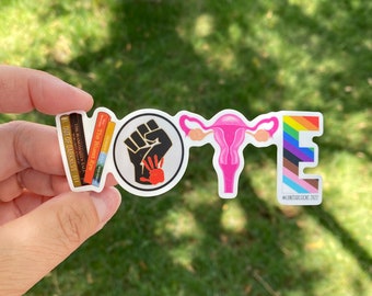 Può includere: Un adesivo con la parola "VOTE" scritta usando diversi simboli. La "V" è una pila di libri, la "O" è un pugno chiuso con un'impronta di mano rossa, la "T" è un utero rosa e la "E" è una bandiera arcobaleno con strisce nere e marroni. L'adesivo ha il testo "#UNITASDESIGNS 2022" in basso.