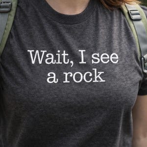 A gray t-shirt with the text "WAIT, I see a rock" printed on it.