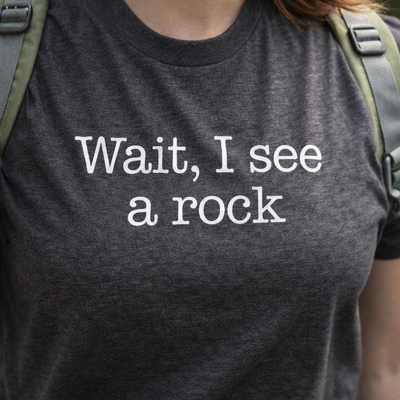 A gray t-shirt with the text "WAIT, I see a rock" printed on it.
