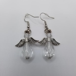 May include: A pair of angel-shaped earrings. Each earring features a clear, faceted teardrop-shaped bead, silver-toned wings, and a small cluster of beads at the top. The earrings hang from silver-toned fish hook ear wires.