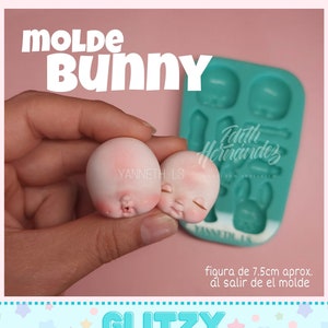 May include: Two small, pale pink bunny head molds with closed eyes and a teal mold in the background. The text "MOLDE BUNNY" is at the top, and "GLITZY MOLDS" is at the bottom. The text "figura de 7.5cm aprox. al salir de el molde" is also visible.