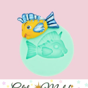 May include: A silicone mold for making a fish-shaped cake decoration. The mold is light green and features a detailed fish design. A yellow and blue fish figurine is shown next to the mold.