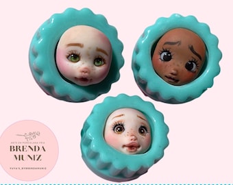 May include: Three porcelain doll heads with painted faces, each head is displayed in a turquoise blue, scalloped, circular frame. The doll heads have different skin tones and facial expressions.