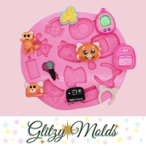 May include: Pink silicone mold with various shapes including a microphone, a backpack, a t-shirt, a camera, a headband, a red panda, and a star. The mold is for making resin crafts.