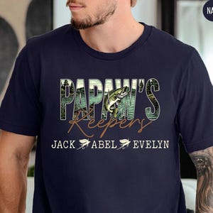 May include: Navy blue t-shirt with the text "PAPAW'S Keepers" in a nature-themed design, featuring a fish graphic. The names "JACK ABEL EVELYN" are printed below the text.