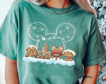 May include: A green t-shirt with a white outline of Mickey Mouse ears. Inside the ears is a gingerbread version of the Disney castle, Mickey Mouse, and other gingerbread treats. The text "SEAFOM" is in the top left corner of the image.