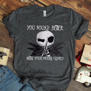 May include: A dark gray t-shirt with a black and white graphic of Jack Skellington from The Nightmare Before Christmas. The graphic shows Jack Skellington with his finger to his lips and the text "You sound better with your mouth closed".
