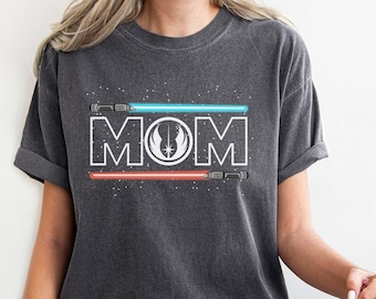 May include: A dark gray t-shirt with a white outline of the word "MOM" and a Star Wars symbol in the middle. The letters are framed by two light sabers, one blue and one red.