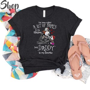 May include: A dark gray t-shirt with a white graphic print of a skeleton couple with the text "I've been called a lot of names in my lifetime but Daddy is my favorite".
