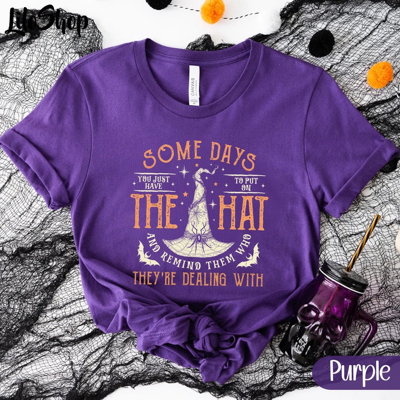 May include: Purple t-shirt with a witch hat graphic and the text "Some days you just have to put on the hat and remind them who they're dealing with".