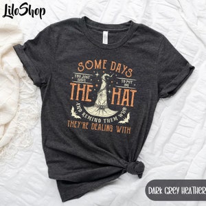 May include: Dark grey heather t-shirt with a graphic of a witch's hat and the text "Some days you just have to put on the hat and remind them who they're dealing with".