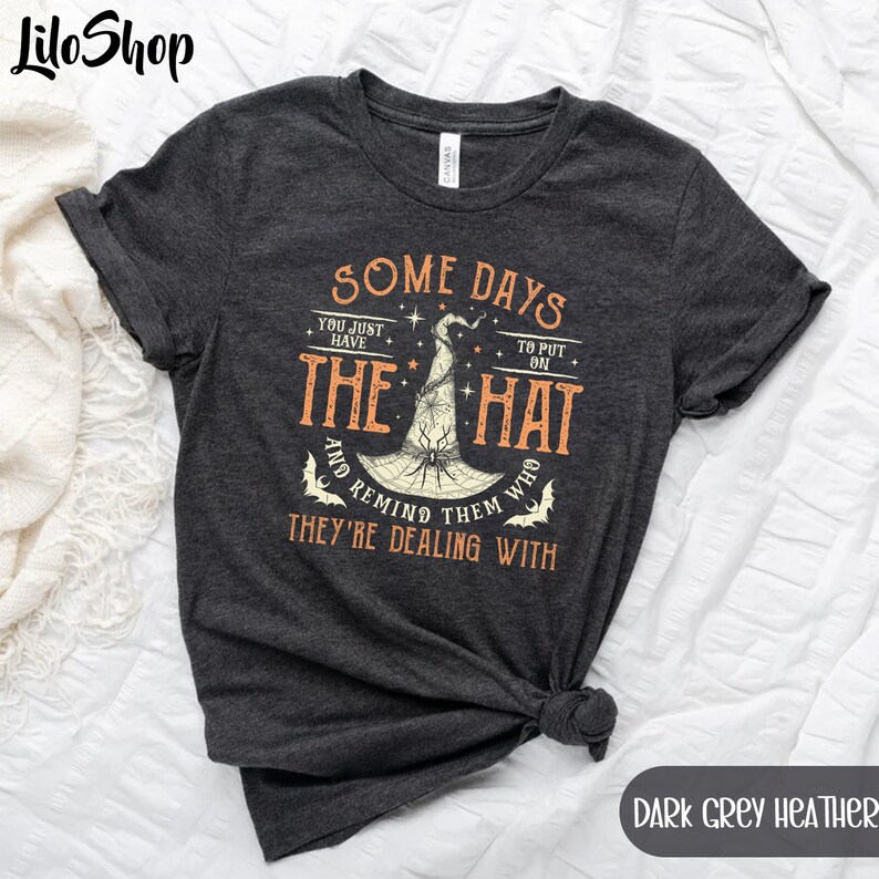 May include: Dark grey heather t-shirt with a graphic of a witch's hat and the text "Some days you just have to put on the hat and remind them who they're dealing with".