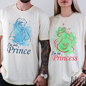 Puede incluir: Dos camisetas color crema. Una presenta una ilustraci&oacute;n azul de un pr&iacute;ncipe con el texto "I'm her Prince". La otra tiene una ilustraci&oacute;n verde de una princesa con el texto "I'm his Princess".