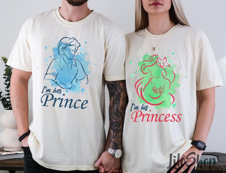 Puede incluir: Dos camisetas color crema. Una presenta una ilustraci&oacute;n azul de un pr&iacute;ncipe con el texto "I'm her Prince". La otra tiene una ilustraci&oacute;n verde de una princesa con el texto "I'm his Princess".