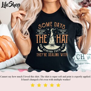 May include: Black t-shirt with a white graphic of a witch's hat with a spider and the text "Some days you just have to put on the hat and remind them who they're dealing with".