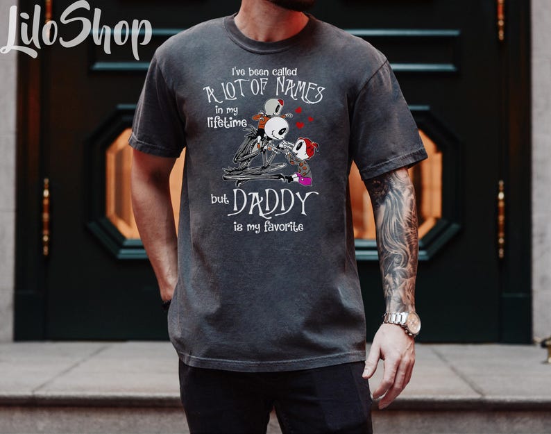 May include: A dark gray t-shirt with a graphic of a skeleton character holding two smaller skeleton characters. The text on the shirt reads "I've been called a lot of names in my lifetime but Daddy is my favorite."
