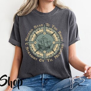 Puede incluir: Una camiseta gris oscuro con un dise&ntilde;o de br&uacute;jula que presenta un barco y el texto "Second Star To The Right & Straight On 'Til Morning".