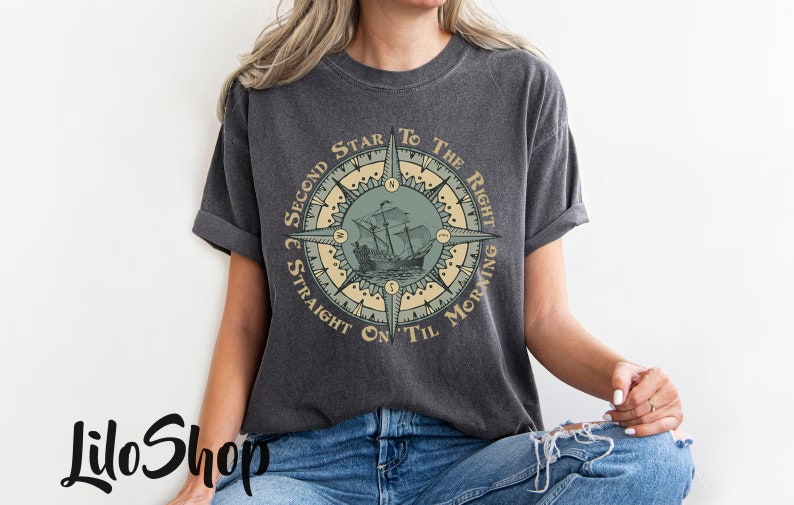 Puede incluir: Una camiseta gris oscuro con un dise&ntilde;o de br&uacute;jula que presenta un barco y el texto "Second Star To The Right & Straight On 'Til Morning".