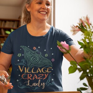 Puede incluir: Una camiseta azul marino con un gr&aacute;fico colorido de una manta raya y el texto "Village Crazy Lady".