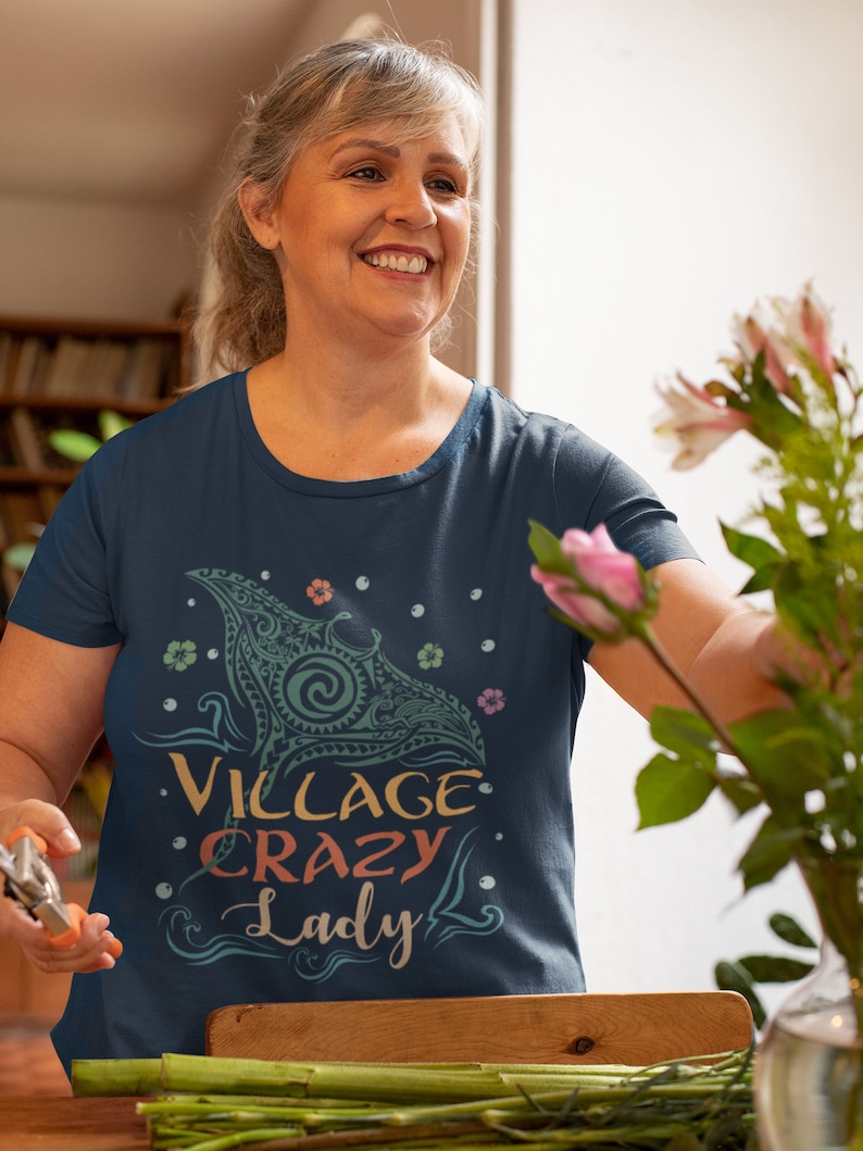Puede incluir: Una camiseta azul marino con un gr&aacute;fico colorido de una manta raya y el texto "Village Crazy Lady".