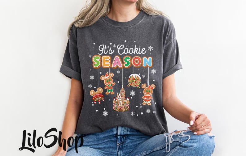 May include: Dark gray t-shirt with the text "It's Cookie SEASON" in colorful letters. The shirt features gingerbread mouse characters and a gingerbread castle. A festive design for the holiday season.