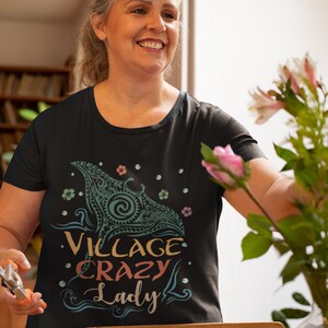 Puede incluir: Una camiseta negra con un gr&aacute;fico colorido de una manta raya y el texto "Village Crazy Lady".