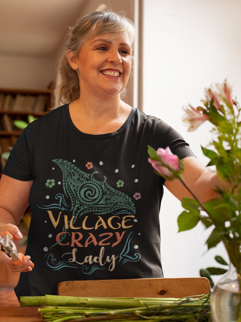 Puede incluir: Una camiseta negra con un gr&aacute;fico colorido de una manta raya y el texto "Village Crazy Lady".