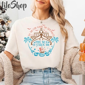 May include: Cream-colored t-shirt with a nautical design. The graphic features a ship, palm trees, and the text "SEE THE LINE WHERE THE SKY MEETS THE SEA IT CALLS ME" in blue and brown. The shirt is a relaxed fit.