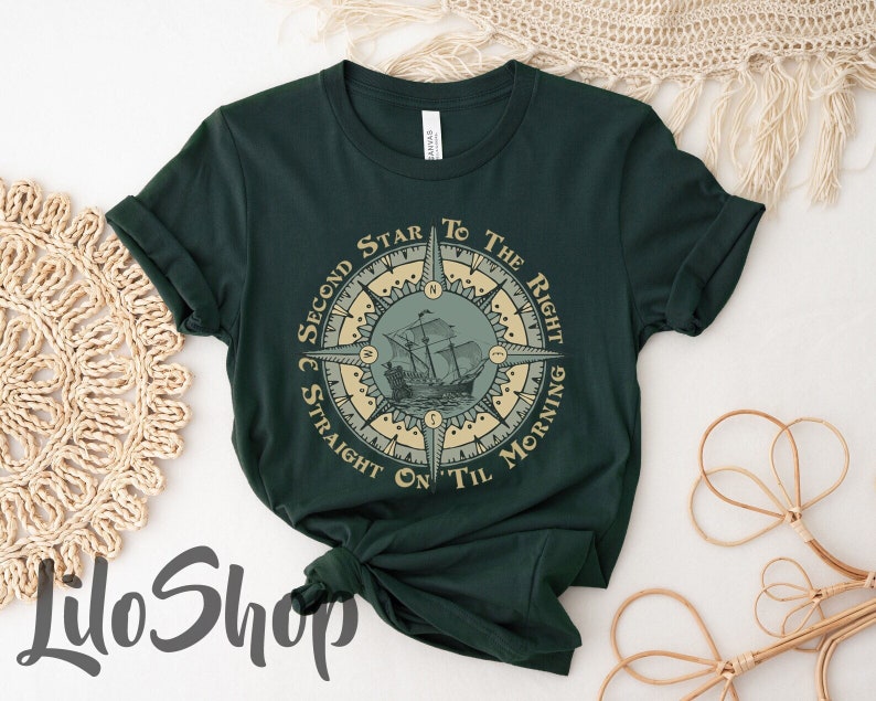 Puede incluir: Una camiseta verde oscuro con un dise&ntilde;o de br&uacute;jula que presenta un barco y el texto "Second Star to the Right and Straight On Til Morning".