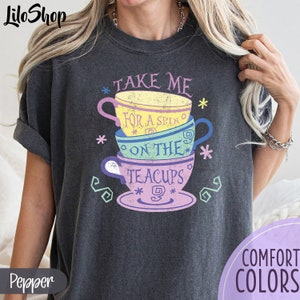 Peut inclure: Un t-shirt gris foncé avec un graphique de tasses à thé empilées et le texte "Take me for a spin on the teacups".