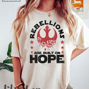 May include: A white t-shirt with a red and black rebel alliance symbol and the text "Rebellions are built on hope".