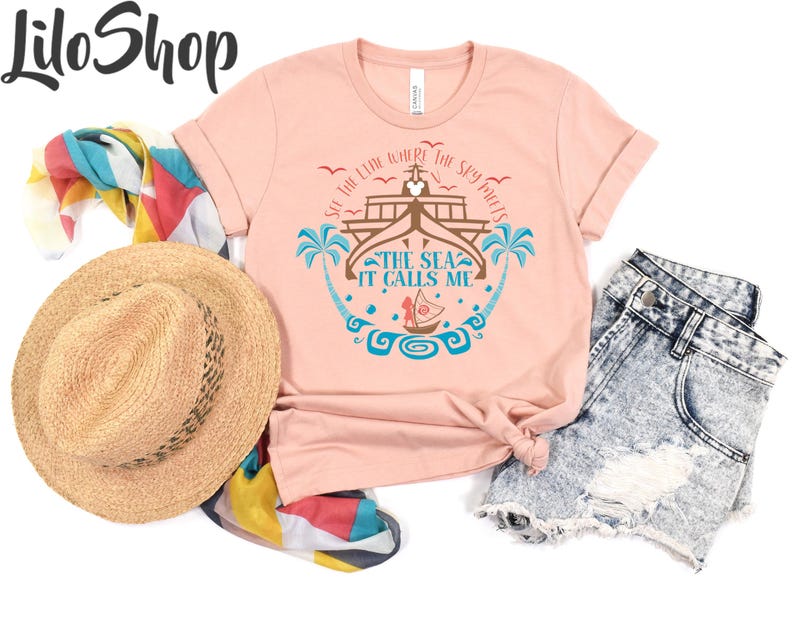 May include: A light pink t-shirt with the text "SEE THE LINE WHERE THE SKY MEETS THE SEA IT CALLS ME" and a graphic of a boat, palm trees, and waves. The shirt is paired with denim shorts, a straw hat, and a colorful scarf.
