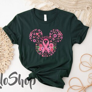 May include: A dark green t-shirt featuring a graphic design shaped like a mouse head silhouette. The design is composed of pink breast cancer awareness ribbons, various pink flowers, and small hearts, with the text Breast Cancer Hope.