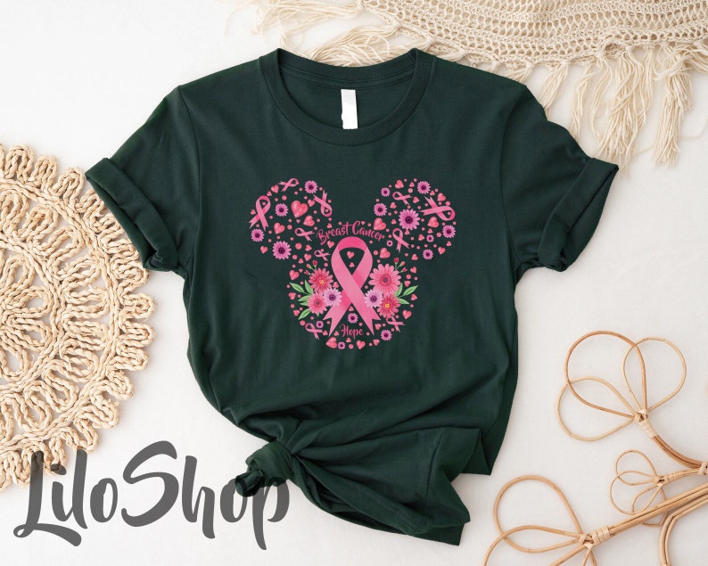 May include: A dark green t-shirt featuring a graphic design shaped like a mouse head silhouette. The design is composed of pink breast cancer awareness ribbons, various pink flowers, and small hearts, with the text Breast Cancer Hope.