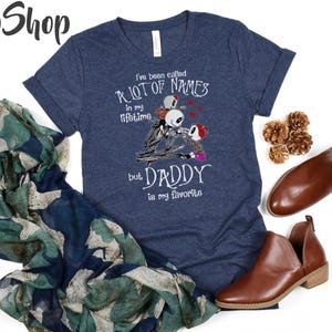 May include: A navy blue t-shirt with a graphic of three skeletons from the Nightmare Before Christmas movie. The text on the shirt reads "I've been called a lot of names in my lifetime but Daddy is my favorite."