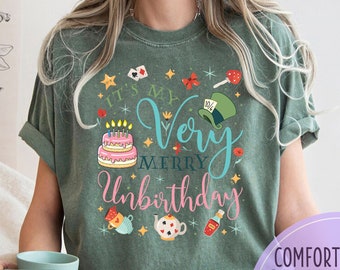 May include: A green t-shirt with a pink and blue graphic that says "It's my very merry unbirthday". The graphic includes a birthday cake, a playing card, a teacup, a teapot, a lollipop, and a hat.