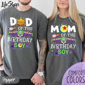 Puede incluir: Dos camisetas grises con un diseño gráfico blanco. El texto en las camisetas dice "Papá del niño de cumpleaños" y "Mamá del niño de cumpleaños". El gráfico es una nave espacial de dibujos animados con una estrella en el lateral.
