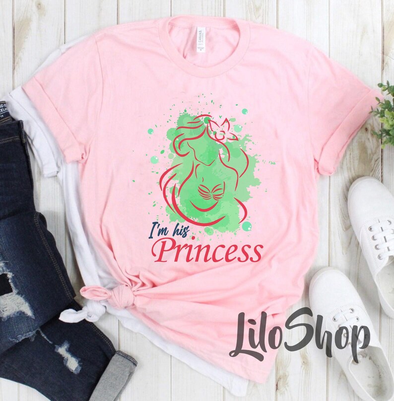 Puede incluir: Camiseta rosa claro con un dise&ntilde;o de sirena verde y roja y el texto "I'm his. Princess". La camiseta tiene cuello redondo y mangas cortas. El nombre de la marca "LiloShop" est&aacute; impreso en la parte inferior.