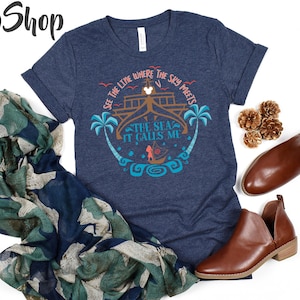 May include: Navy blue t-shirt with a graphic design featuring the text "See the line where the sky meets the sea, it calls me." The design includes palm trees, a boat, and a ship. The shirt is paired with brown shoes and a patterned scarf.