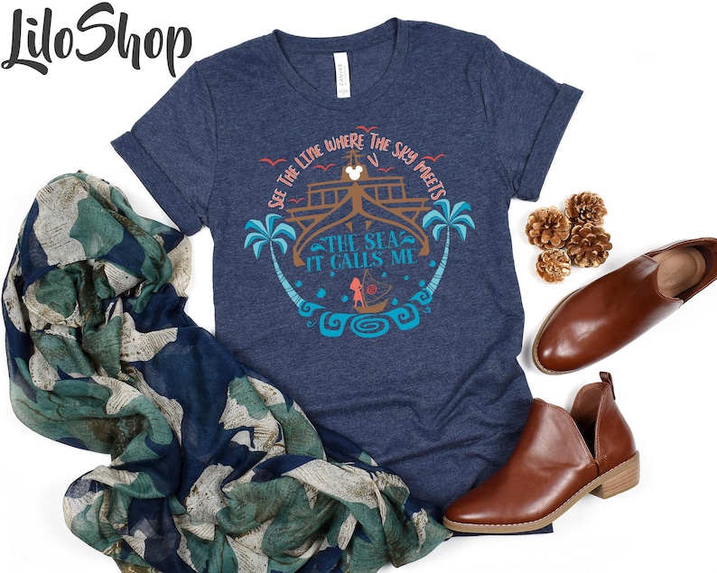 May include: Navy blue t-shirt with a graphic design featuring the text "See the line where the sky meets the sea, it calls me." The design includes palm trees, a boat, and a ship. The shirt is paired with brown shoes and a patterned scarf.
