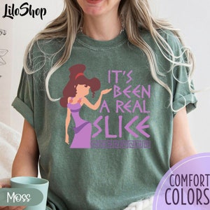May include: A green t-shirt with a cartoon image of a woman with brown hair and a purple dress. The text "It's Been A Real Slice" is printed on the shirt in purple and white.