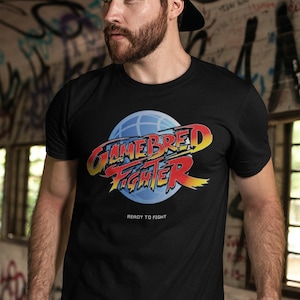 Puede incluir: Una camiseta negra con un gráfico rojo y amarillo de un globo terráqueo con el texto "Gamebred Fighter" y las palabras "Ready to Fight" debajo.