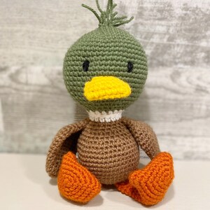 May include: A crocheted duck toy with green and brown body, yellow beak, and orange feet.