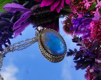 May include: A silver chain necklace with a large oval pendant featuring a blue and green labradorite gemstone. The pendant has a silver filigree border.