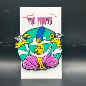 May include: A yellow and blue enamel pin featuring a parody of the famous painting "The Birth of Venus" with characters from the animated television show "The Simpsons". The pin features the text "The Pindy's" at the top.