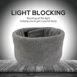 May include: Gray sleep mask made of soft fabric, designed to block out light. The mask is shaped like a cylinder and has a padded interior. The text "LIGHT BLOCKING" is displayed above the mask, with the tagline "Blocking all the light helping you to get a sound sleep".