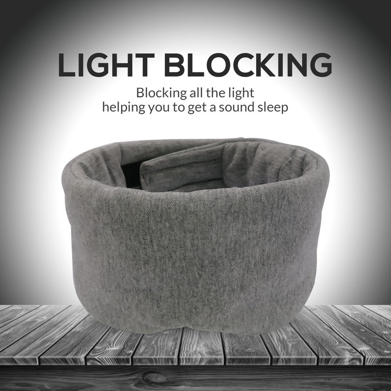 May include: Gray sleep mask made of soft fabric, designed to block out light. The mask is shaped like a cylinder and has a padded interior. The text "LIGHT BLOCKING" is displayed above the mask, with the tagline "Blocking all the light helping you to get a sound sleep".