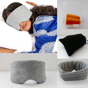May include: A gray sleep mask with a contoured shape for comfortable eye coverage. The mask is made of a soft, breathable fabric. Also pictured are a pair of orange earplugs in a plastic container and a black velvet pouch.